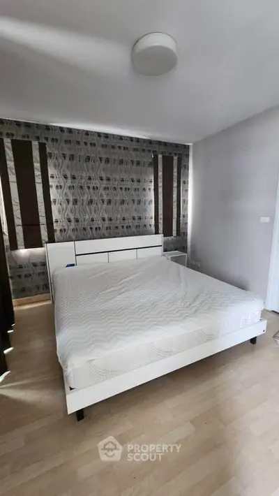 Spacious bedroom with modern decor and stylish wallpaper, featuring a comfortable bed and ample natural light.