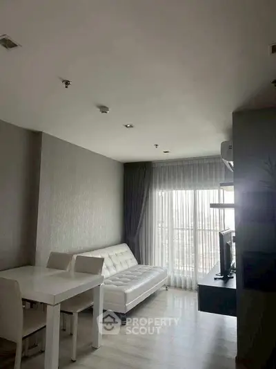 Modern living room with white sofa and dining area, featuring large windows and natural light.