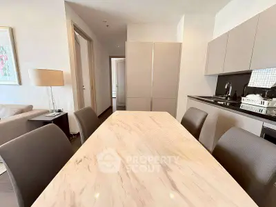 Modern dining area with sleek marble table and stylish kitchen in open layout apartment.