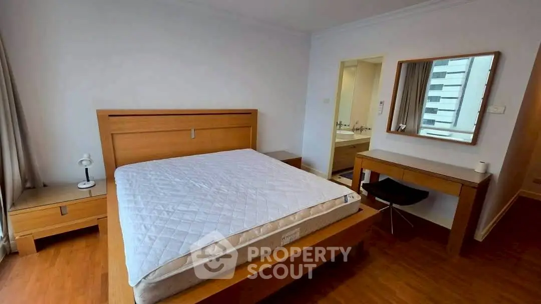 Spacious bedroom with modern wooden furniture and ensuite bathroom in a high-rise apartment.