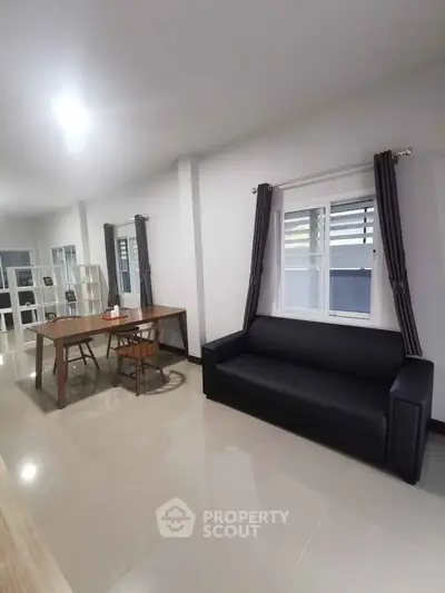 Spacious modern living room with sleek black sofa and elegant dining area, perfect for entertaining.