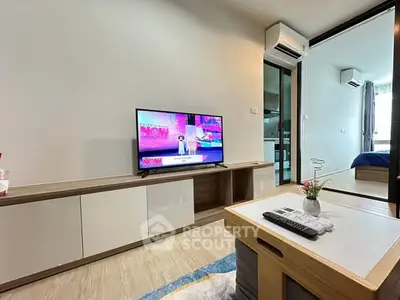 Modern living room with sleek furniture and TV, open layout to bedroom