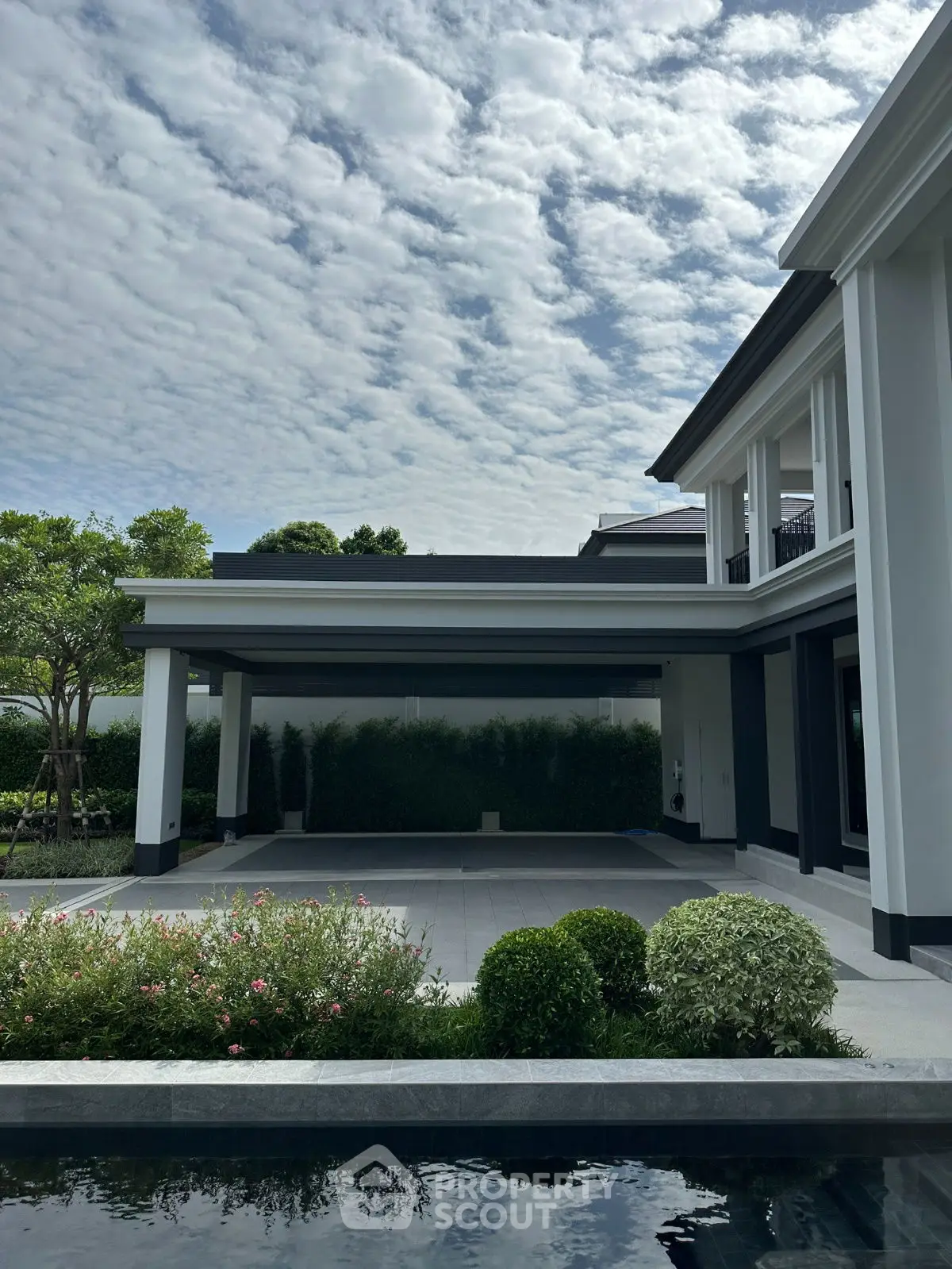 Luxurious modern home exterior with elegant landscaping and spacious driveway under a cloudy sky.