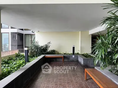 Modern building entrance with greenery and seating area, offering a welcoming atmosphere.