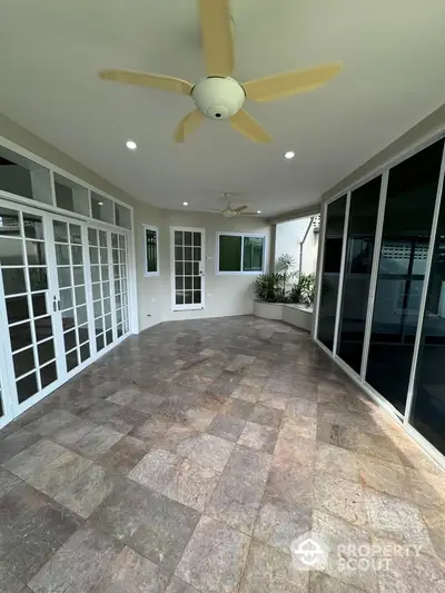 Spacious enclosed balcony with ceiling fan and tiled flooring, perfect for relaxation.