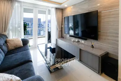 Modern living room with large TV, sleek furniture, and natural light from balcony.
