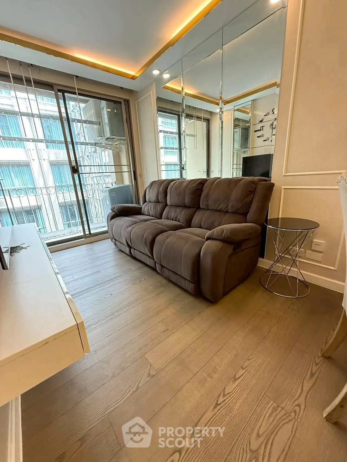 Modern living room with cozy sofa and mirrored wall, featuring elegant wood flooring and balcony access.