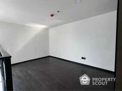 Spacious empty room with dark wood flooring and white walls, perfect for customization.