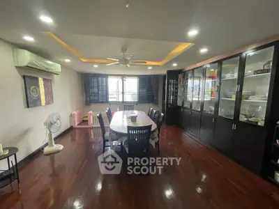 Spacious dining area with polished wooden floors, large dining table, and ample cabinetry, complemented by natural light and modern ceiling fan.