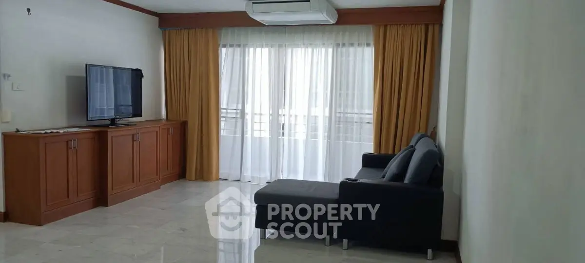 Spacious living room with modern sofa and large TV, featuring elegant curtains and natural light.