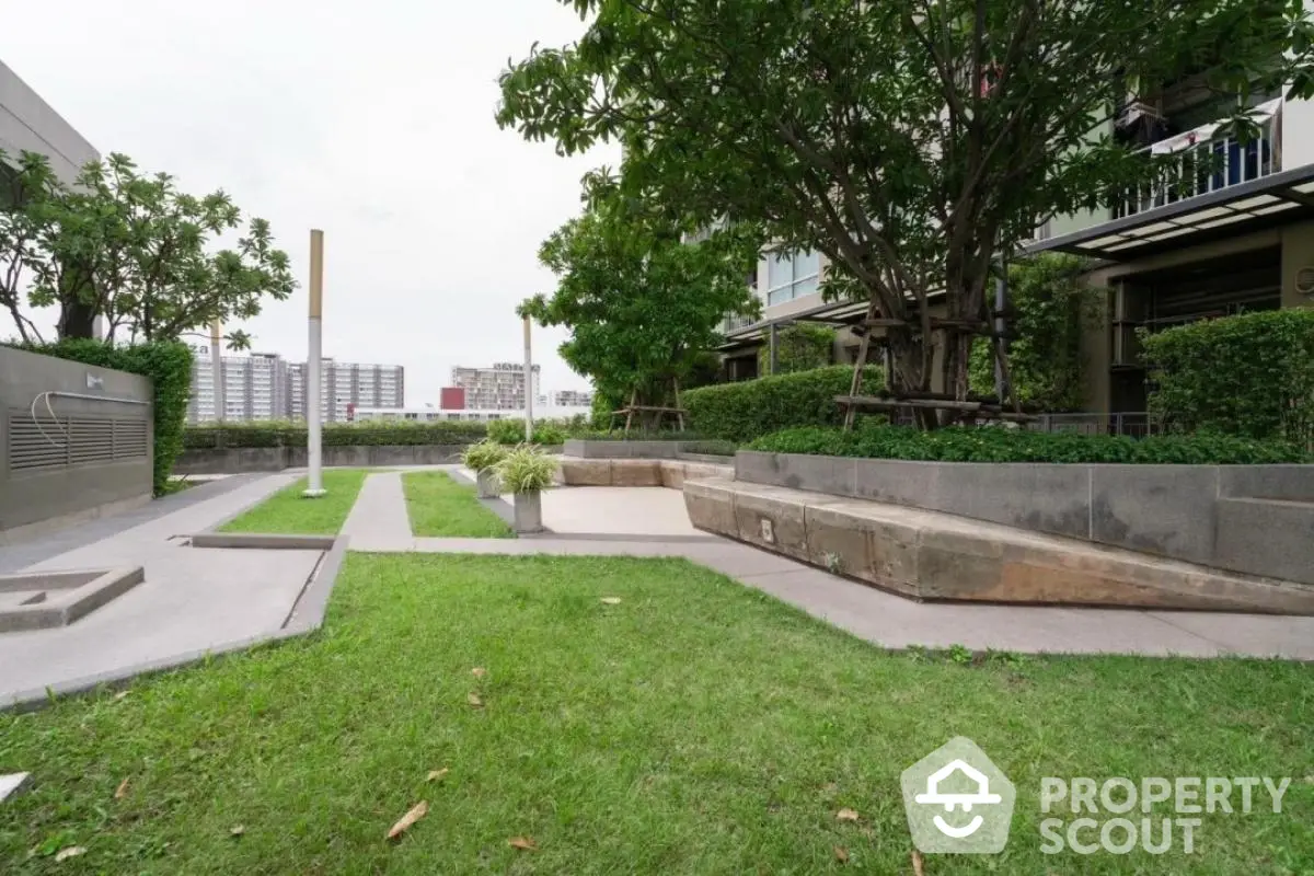 Spacious garden area in modern residential complex with lush greenery and seating