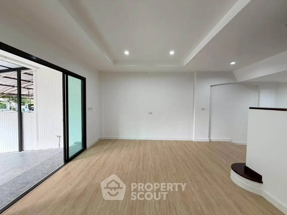 Spacious modern living room with wooden flooring and large sliding glass doors opening to a patio.