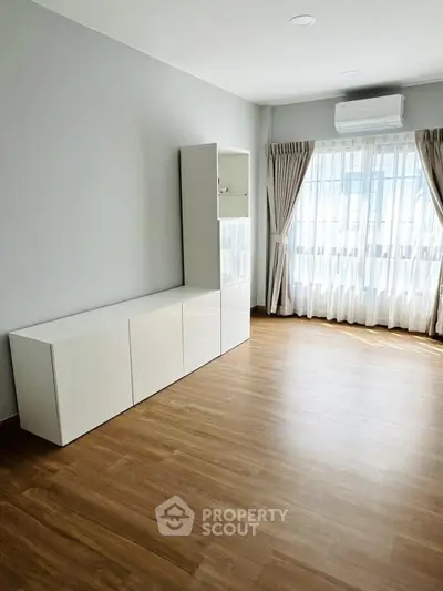 Spacious empty room with wooden flooring and large window, perfect for customization.