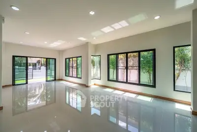 Spacious modern living room with large windows and glossy tiled floors, offering abundant natural light and garden views.