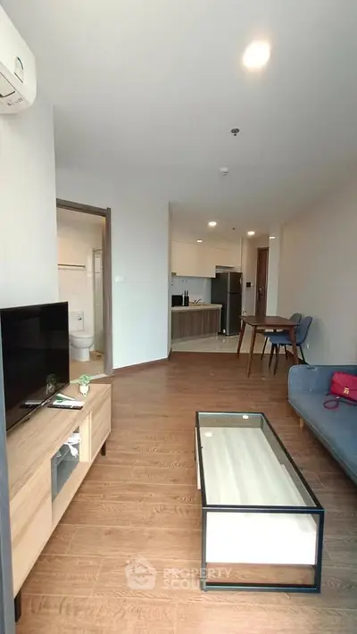 Modern living room with wooden flooring, stylish furniture, and open kitchen layout in a contemporary apartment.