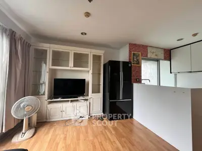 Modern living room with wooden flooring, TV unit, and sleek black refrigerator in open layout.