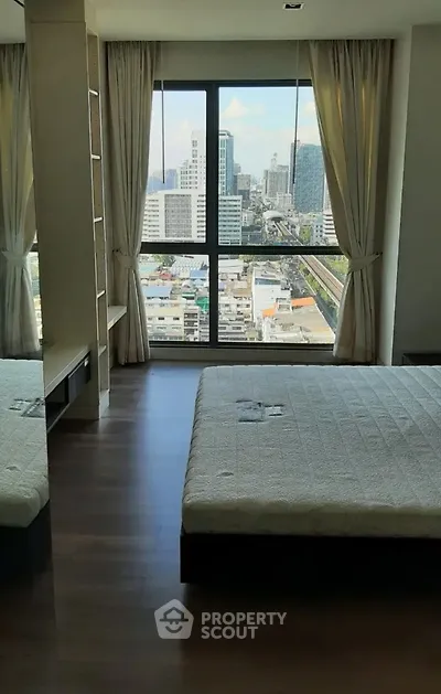 Spacious bedroom with stunning city view from large window in modern high-rise apartment.