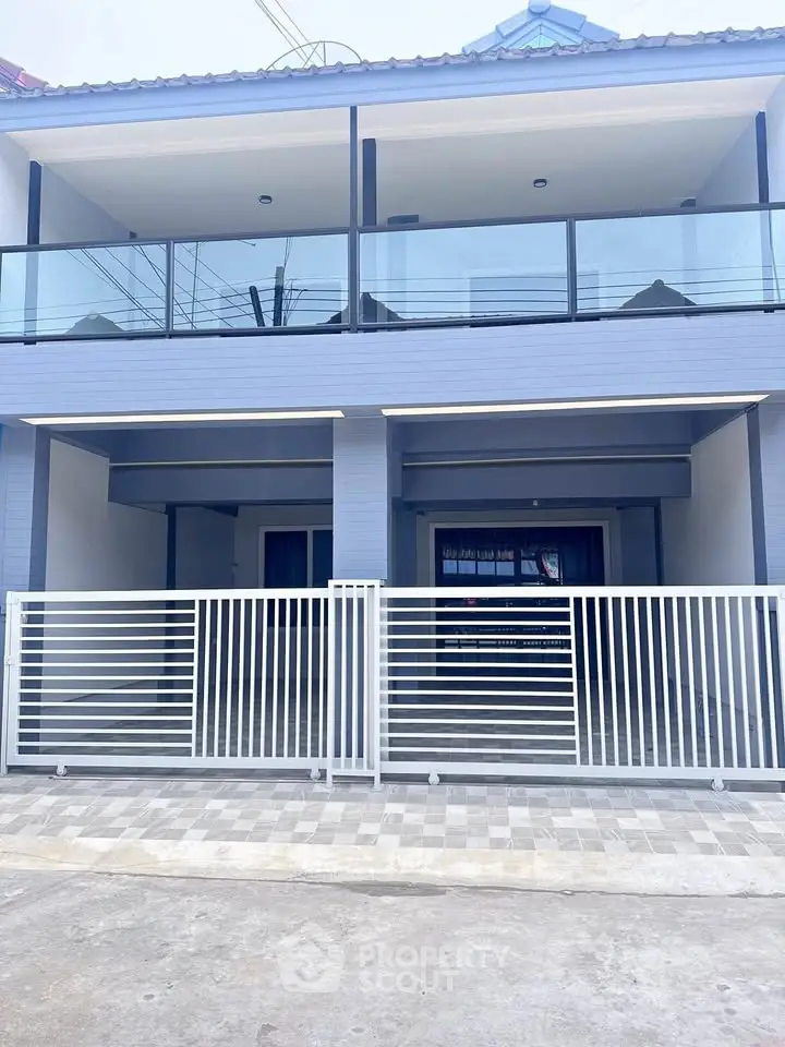 Modern two-story house with sleek glass balcony and gated entrance, perfect for contemporary living.