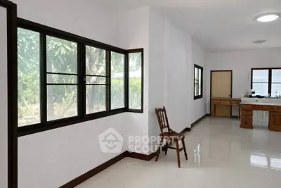 Spacious interior with large windows and natural light, featuring a simple wooden chair and tiled flooring.