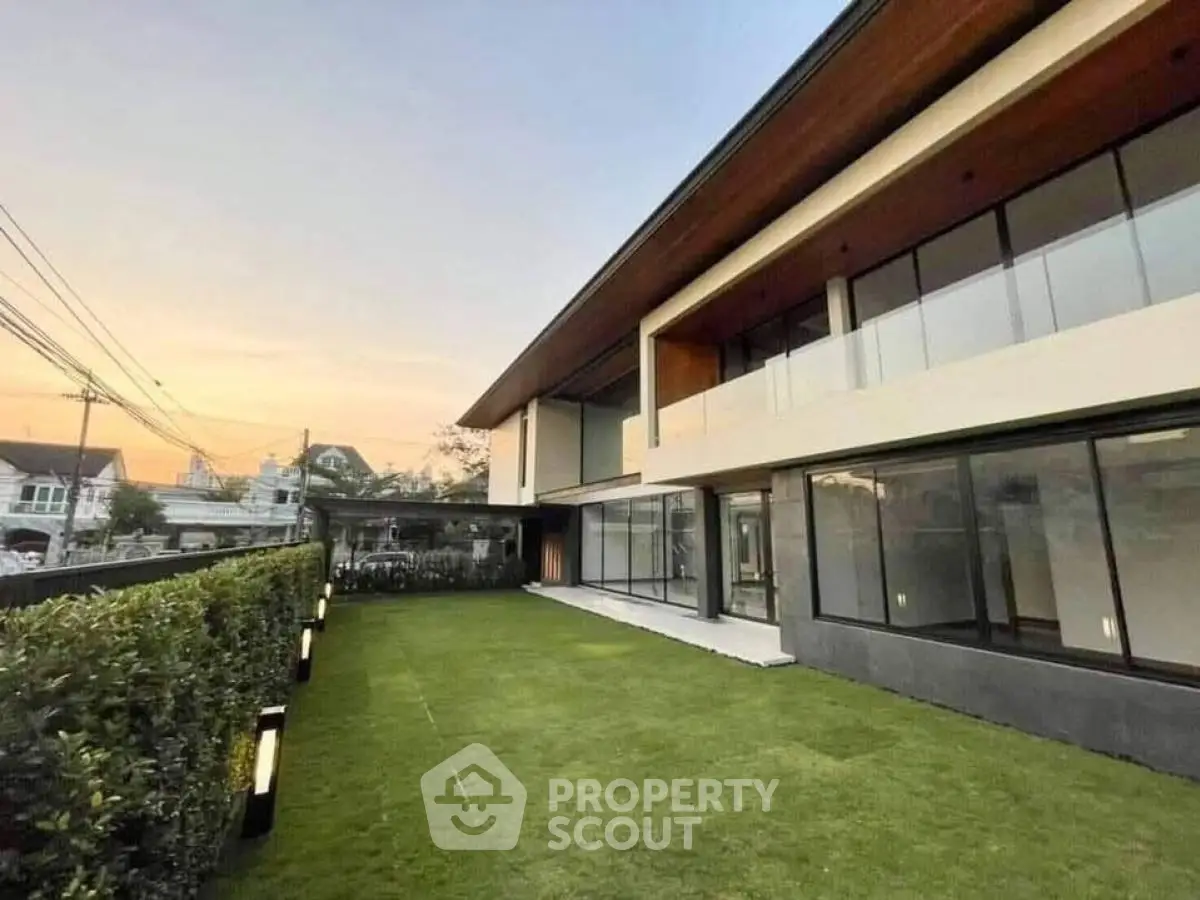 Modern two-story house with large windows and spacious lawn at sunset.