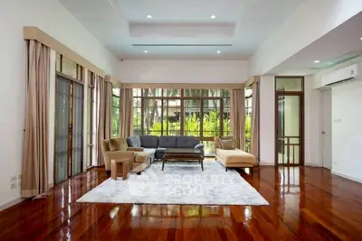 Spacious living room with large windows and garden view, featuring elegant wooden flooring and modern furniture.