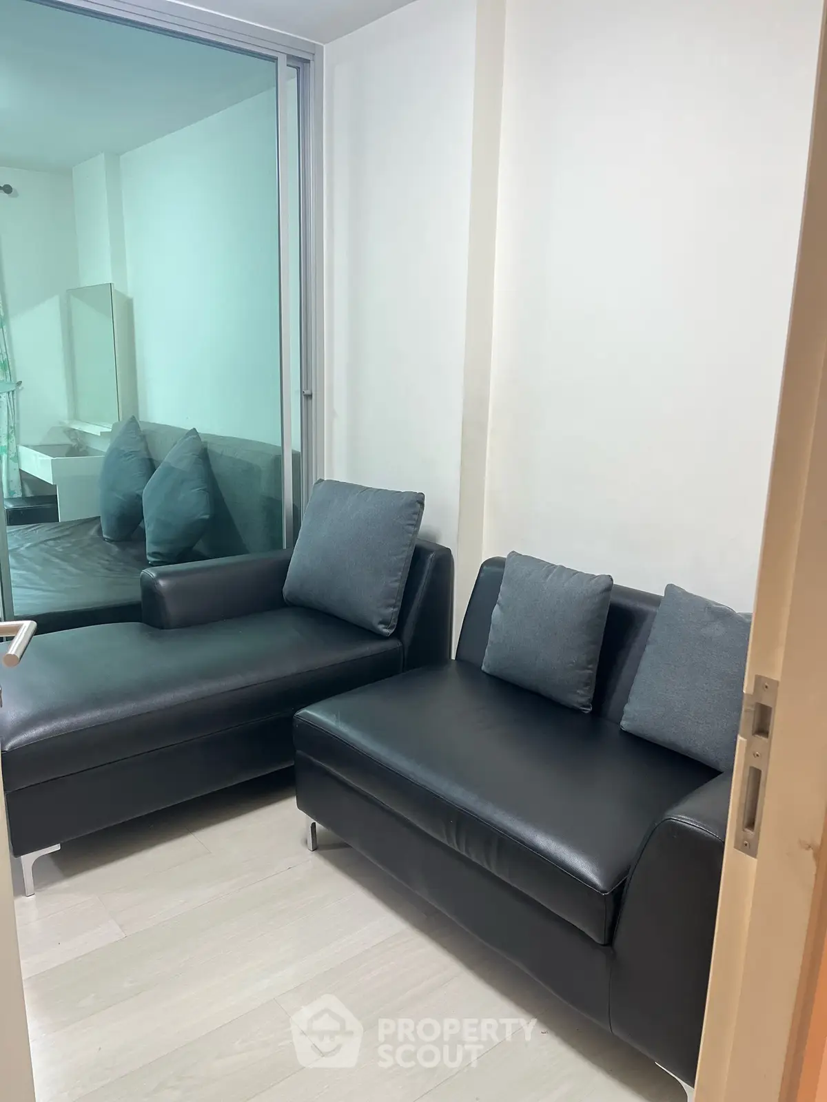 Modern living room with sleek black leather sofas and glass partition, perfect for urban living.