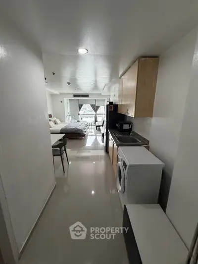 Modern studio apartment with sleek kitchen and cozy living area, featuring a washing machine and city view.