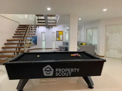 Spacious modern living room with pool table and stylish staircase, perfect for entertainment.