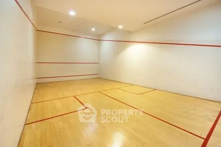 Spacious indoor squash court with wooden flooring and bright lighting.