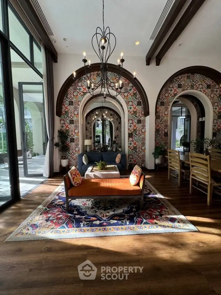 Luxurious living room with elegant chandelier and vibrant decor, featuring large windows and stylish furniture.