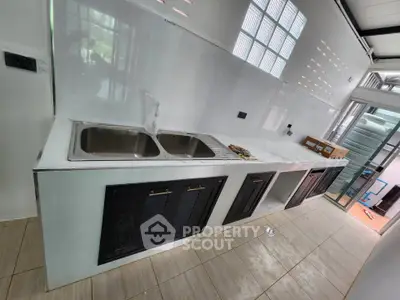 Modern kitchen with sleek countertops and dual sink, featuring ample storage and natural light.