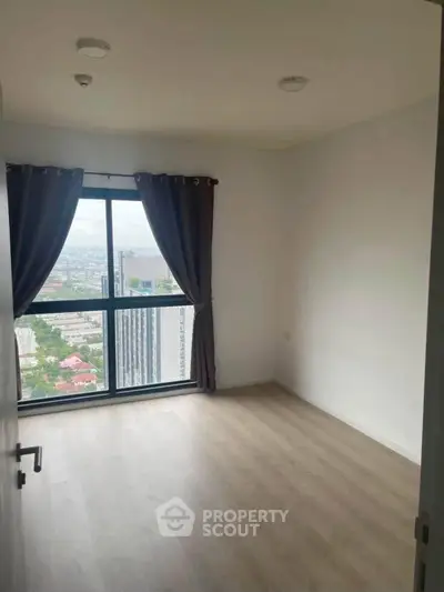Spacious bedroom with large window offering stunning city views in modern high-rise apartment.