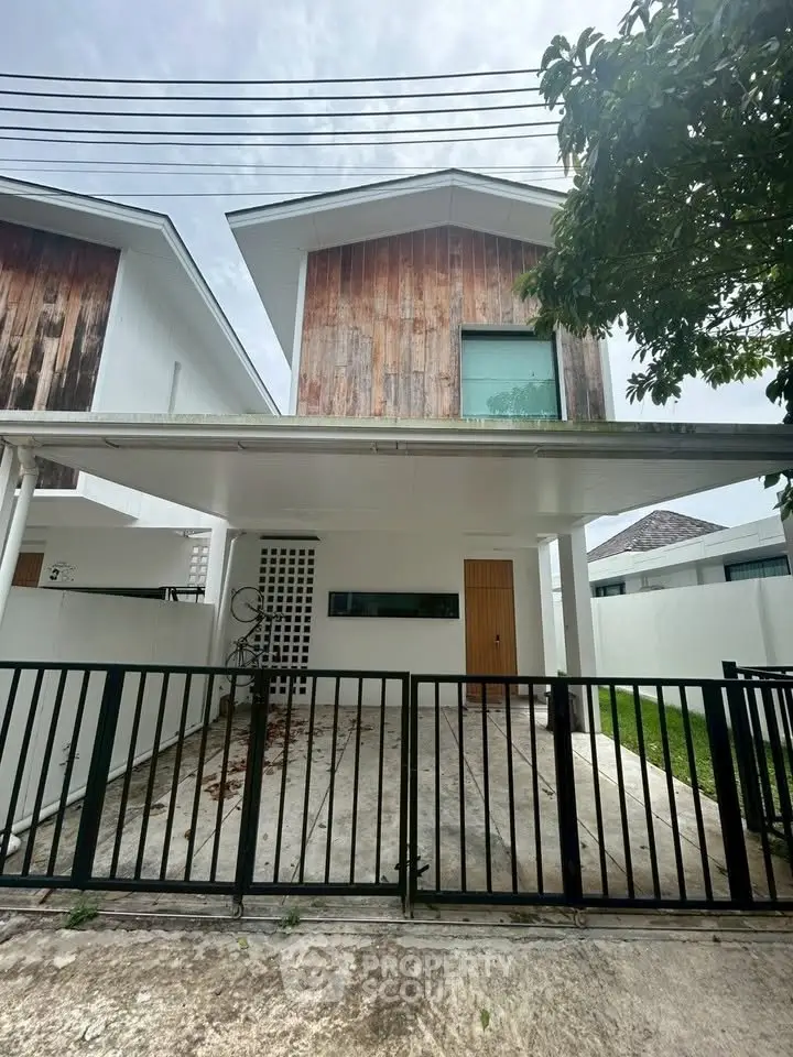 Modern two-story house with wooden facade and gated driveway in a serene neighborhood.
