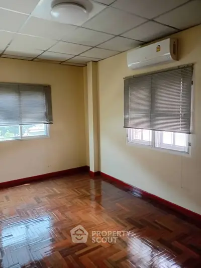 Spacious empty room with polished wooden floors and air conditioning, perfect for customization.