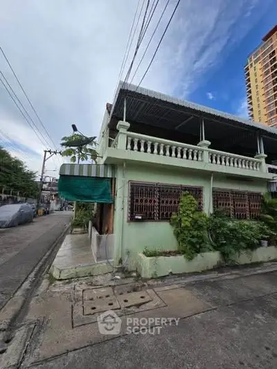 Charming corner unit house with balcony and lush greenery in urban neighborhood.