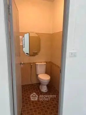 Compact bathroom with tiled floor and wall-mounted mirror, featuring a standard toilet.