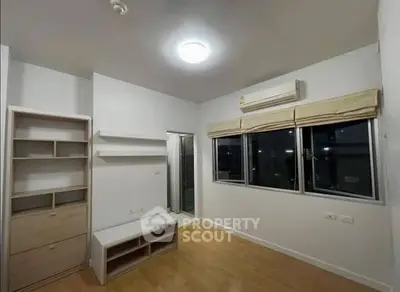 Modern bedroom with wooden flooring and large window, featuring built-in shelves and air conditioning.