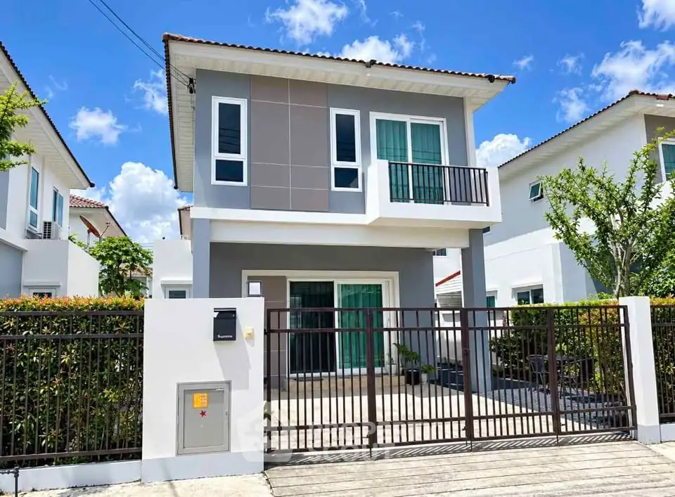 Modern two-story house with balcony and gated driveway under a clear blue sky.