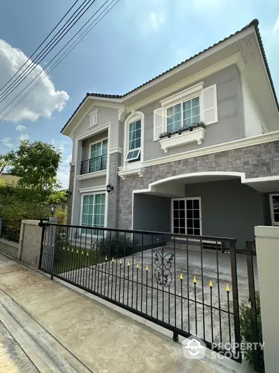 Charming two-story house with elegant facade and gated driveway in sunny suburban neighborhood.