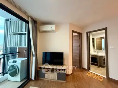 Modern living room with balcony and washing machine, featuring sleek TV setup and wooden flooring.