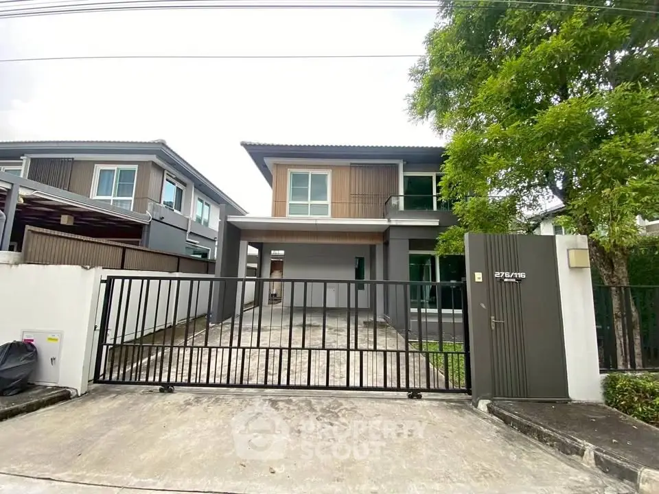 Modern two-story house with gated driveway and lush greenery, perfect for family living.