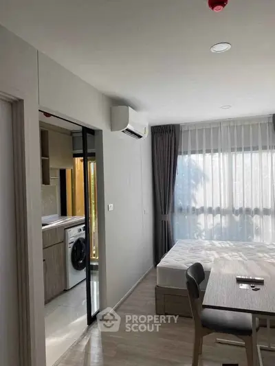 Modern bedroom with natural light and adjacent kitchen area in a stylish apartment.