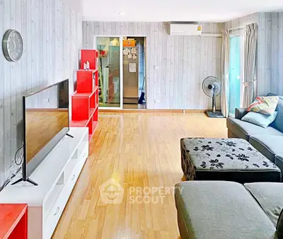 Spacious living room with modern decor and wooden flooring, featuring a large TV and vibrant red shelving.