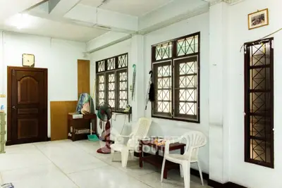 Spacious living area with natural light and simple furnishings, featuring large windows and tiled flooring.