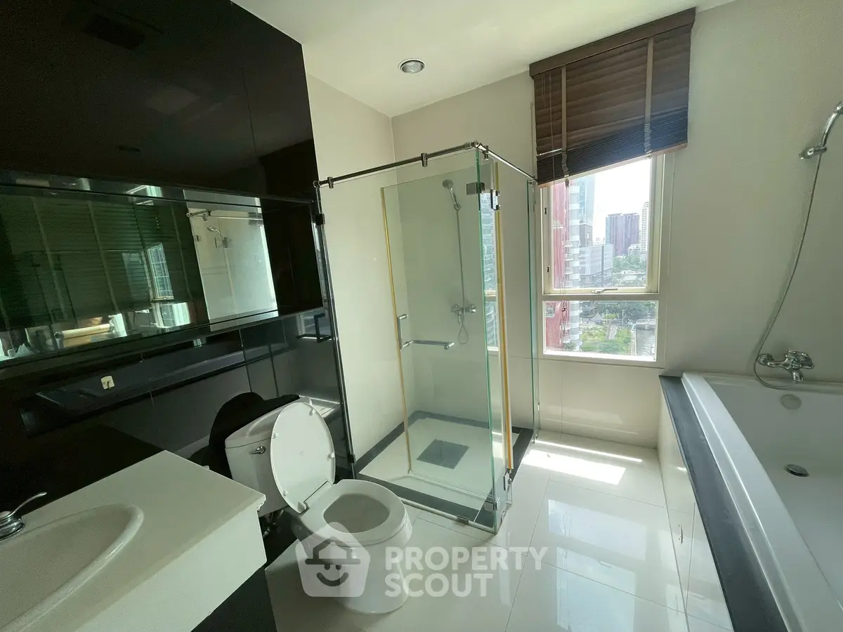 Modern bathroom with glass shower, bathtub, and city view window.