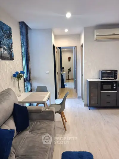 Modern living room with cozy gray sofa, dining table, and compact kitchen appliances.
