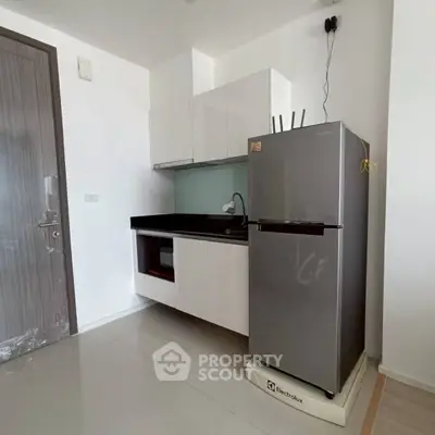 Modern kitchen with sleek cabinetry and stainless steel fridge in a minimalist apartment.