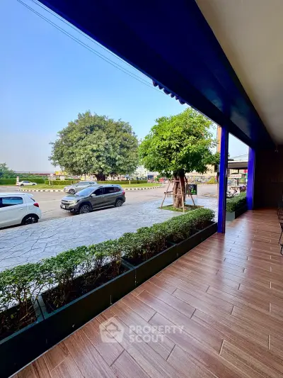 Spacious outdoor terrace with tiled flooring and lush greenery, offering a serene view of the street and trees.