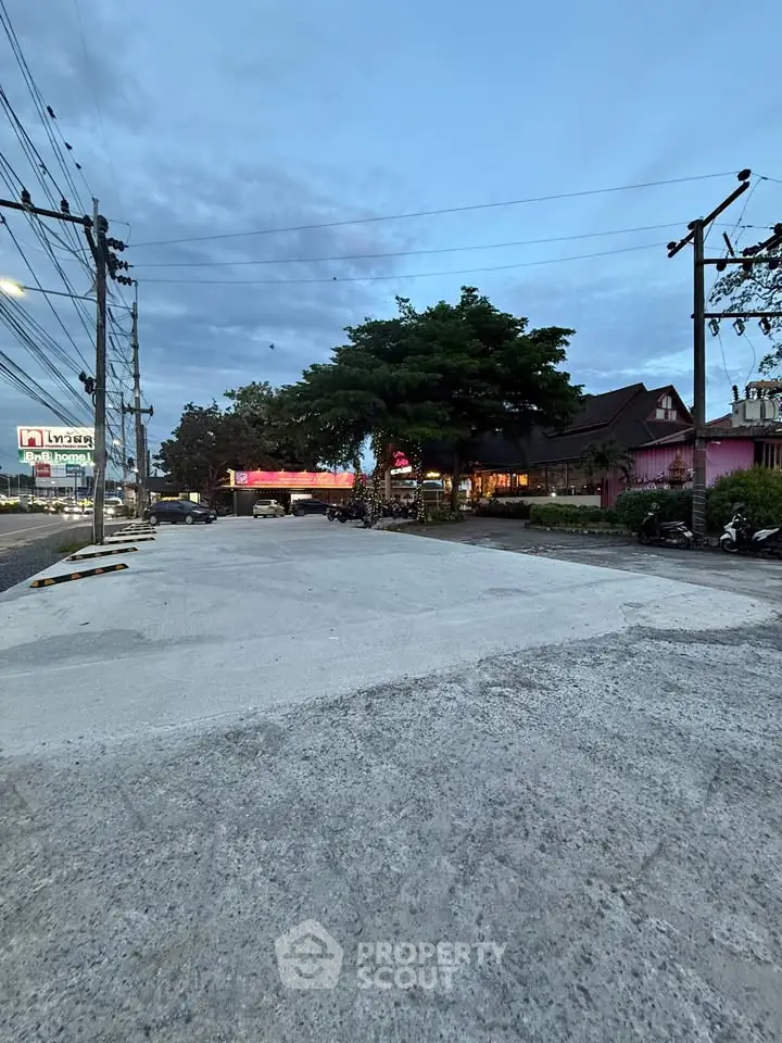 Spacious outdoor area with paved surface and surrounding greenery, ideal for commercial development.