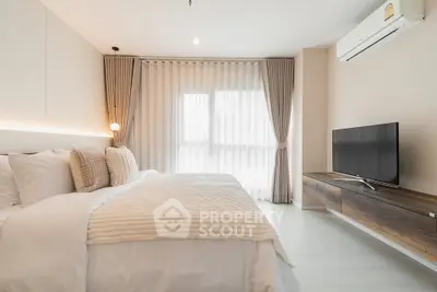 Modern bedroom with cozy bedding, large window, and sleek TV setup, perfect for relaxation and comfort.